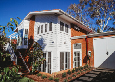 Exterior facade of the extended kitchen with external staircase. Materials are white weatherboard and matching canberra red bricks to tie in with the existing garage and facade.