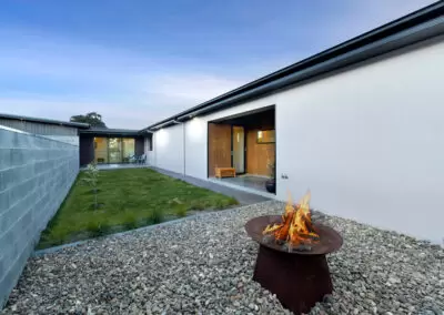 Protected rear courtyard with walling and house on either end. Bright green grass and fireplace in foreground.
