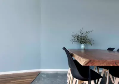 Dining table with blue wall behind. Floor is conrete and timber with elegant black junction.
