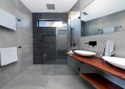 En suite with feature black tiles and highlight window in the shower space. Sinks in foreground.