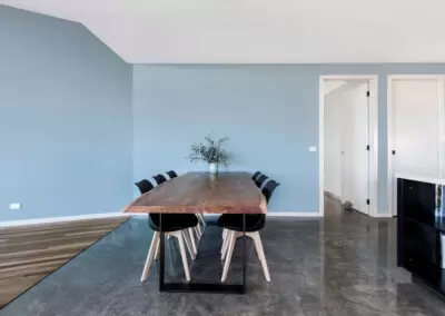 Dining table with blue wall behind. Floor is conrete and timber with elegant black junction.