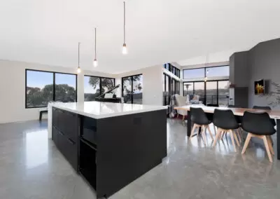 Open pan kitchen, dining and loungeroom with rural views beyond. Three pendants hanging over the kitchen bench.