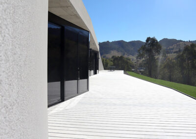Facade of a contemporary house showing bushland reflected in the floor to ceiling glazing and a gleaming white deck