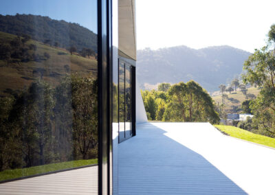Facade of house reflecting the rural landscape. White deck gleaming in the bright sun.