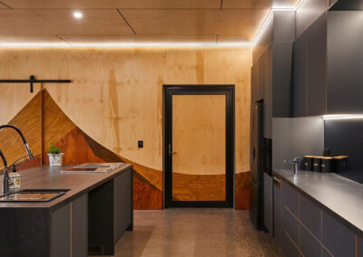 Dark kitchen with timber feature wall beyond.