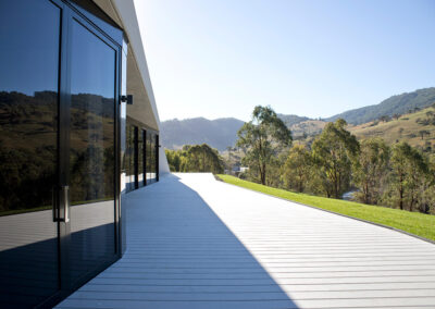 Facade of house reflecting the rural landscape. White deck gleaming in the bright sun.