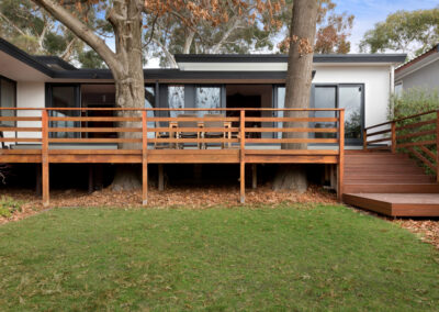 Exterior of Neville Gruzman's midcentury modern house. New deck and extended facade are visible. There is a tree growing through the timber deck.