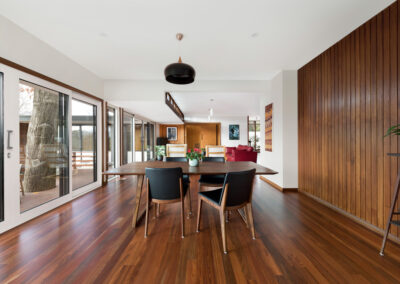 Living and dining room of a midcentury house. Dark pendant hangs over dining table. Extension is in foreground, heritage building fabric in background.