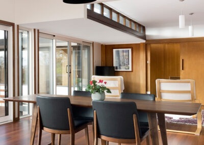 Living and dining room of a midcentury house. Dark pendant hangs over dining table.