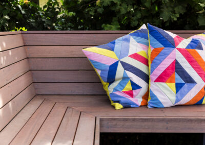 Detail of a built-in timber bench with brightly coloured cushions. Garden surrounds.