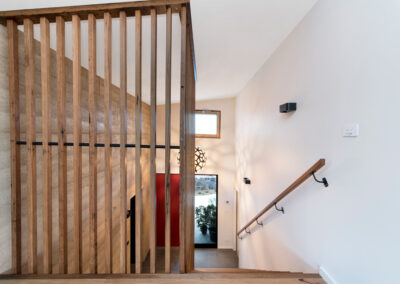 Timber Joinery in the stairwell of our Rammed Earth House project, Canberra. Rammed earth wal can be seen behind timber and red front door beyond that. Pendant glows downstairs.