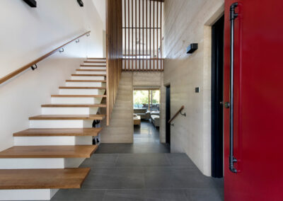 Entry foyer with timber staircase and rammed earth walls. Red front door also visible.