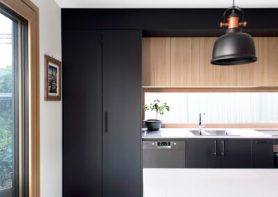 Detail of kitchen with timber and black cabinetry, white benchtops and a pendant hanging in the foreground.