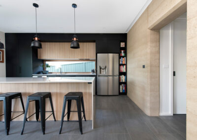 Kitchen with timber and black cabinetry. Rammed earth wall beside.