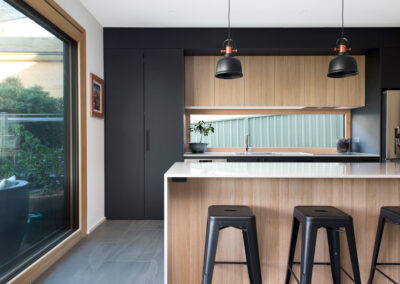Kitchen with timber and black cabinetry. A window over the bench and two pendants hang from the ceiling. Large glass door to the side.