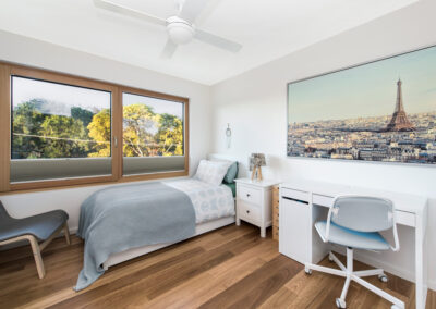 Upstairs bedroom with bed and desk and large windows overlooking leafy canberra suburbs.