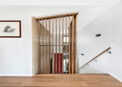 Timber Joinery in the stairwell of our Rammed Earth House project, Canberra. Rammed earth wal can be seen behind timber and red front door beyond that.